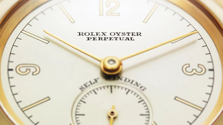 Close-up of a Rolex Oyster Perpetual watch face with gold hands and hour markers.