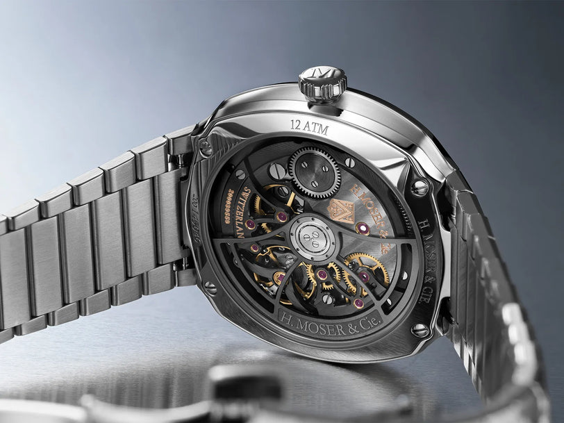 Stainless steel watch with midnight blue fumé dial, visible skeleton caseback showing gold and red mechanical movement, and m