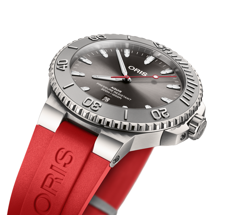 An Oris Aquis Date Relief dive watch in silver with a red strap and black dial, angled to highlight its details.