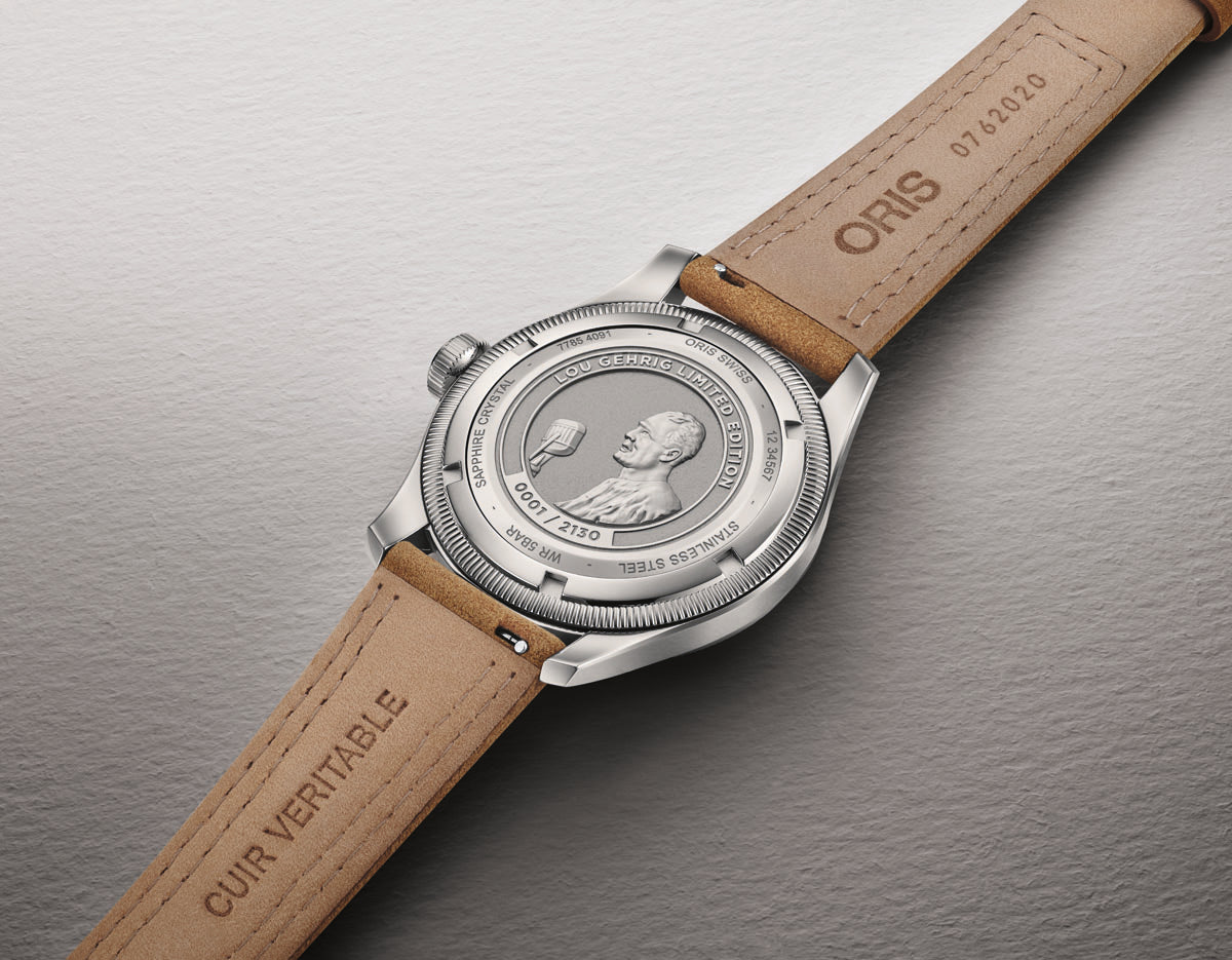 Stainless steel watch with tan leather strap and medallion caseback featuring a profile portrait and engraved text.