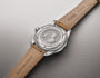 Stainless steel watch with tan leather strap and medallion caseback featuring a profile portrait and engraved text.