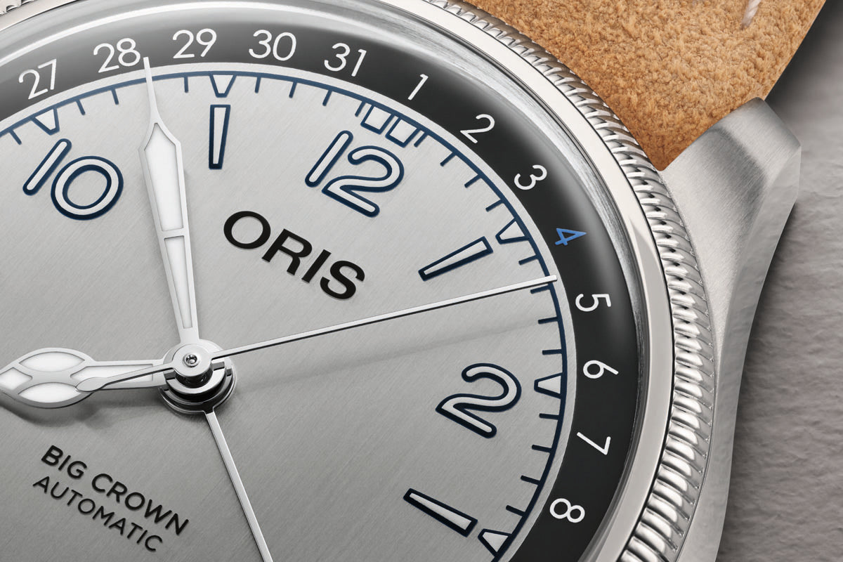 Oris Big Crown Automatic watch with silver dial, blue numerals, date window, and stainless steel case with cork strap detail.