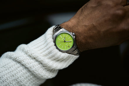 A person wearing a silver wristwatch with a bright green face and a white knit sweater.