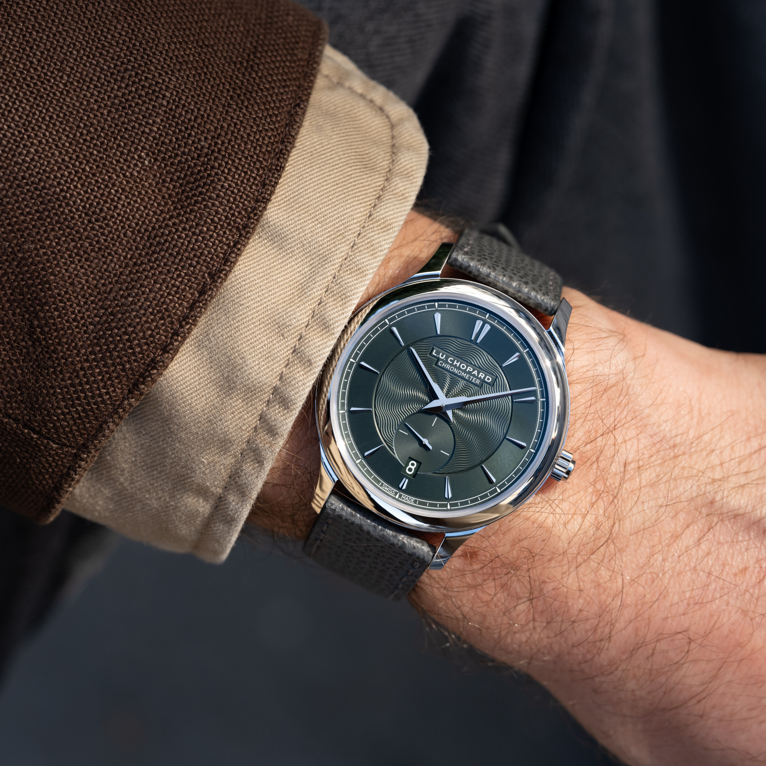A wrist wearing the Chopard L.U.C XPS 1860 Officer Limited Edition For Hodinkee—silver and black—paired with a brown jacket and beige shirt.