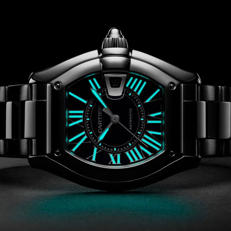 Tonneau-shaped watch with luminous cyan Roman numerals, black dial, two-tone metal bracelet, and crown protector on black bac