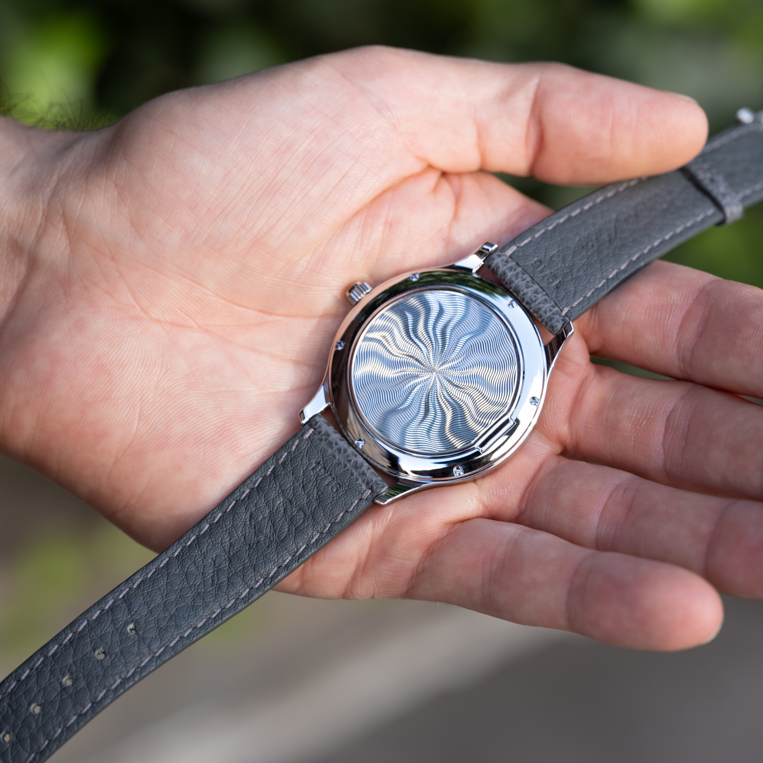 A person holds a Chopard L.U.C XPS 1860 Officer Limited Edition For Hodinkee, showing its intricate swirling guilloché back and grey leather strap.