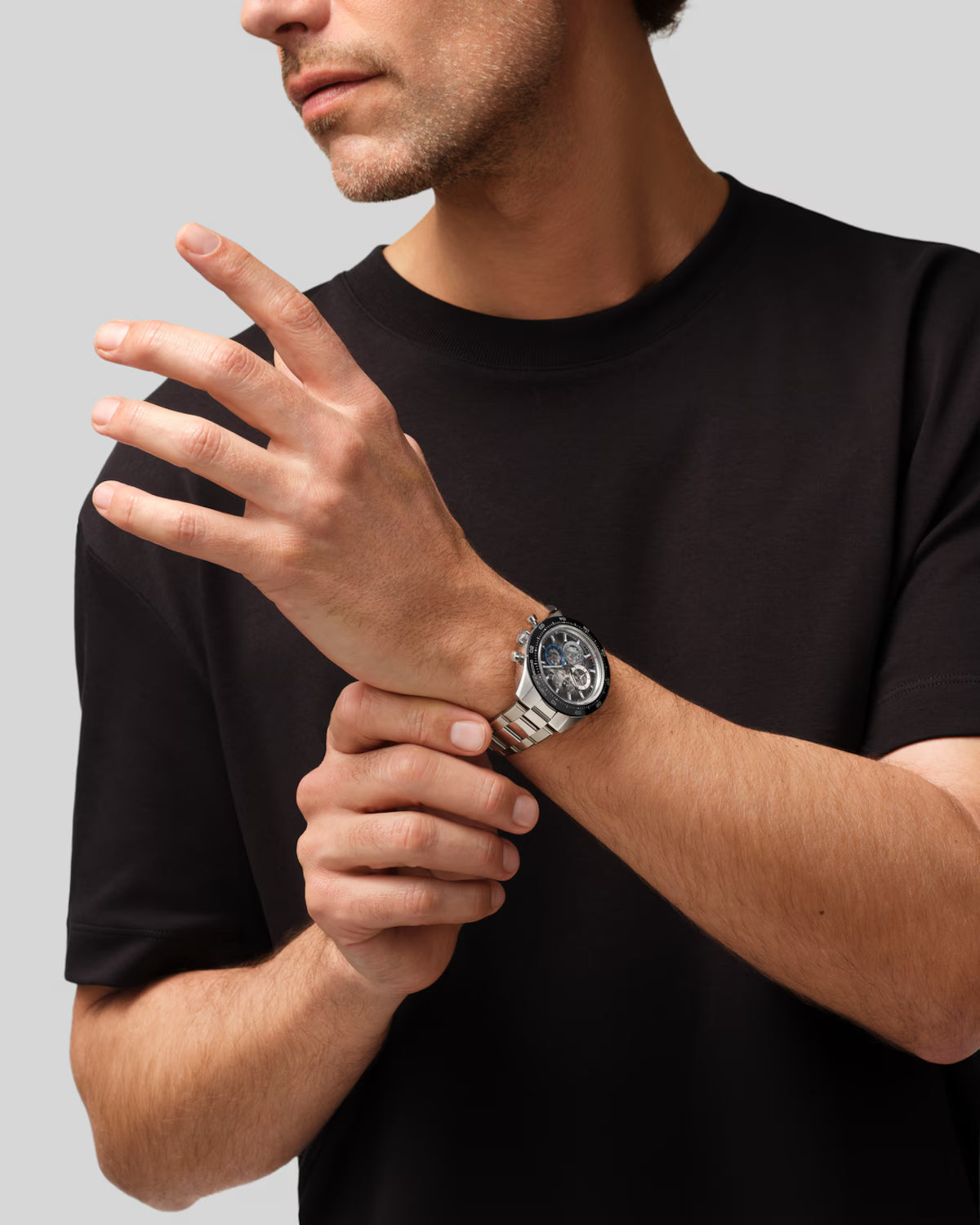 Man wearing black t-shirt with silver chronograph watch on wrist with dark dial and metal band.