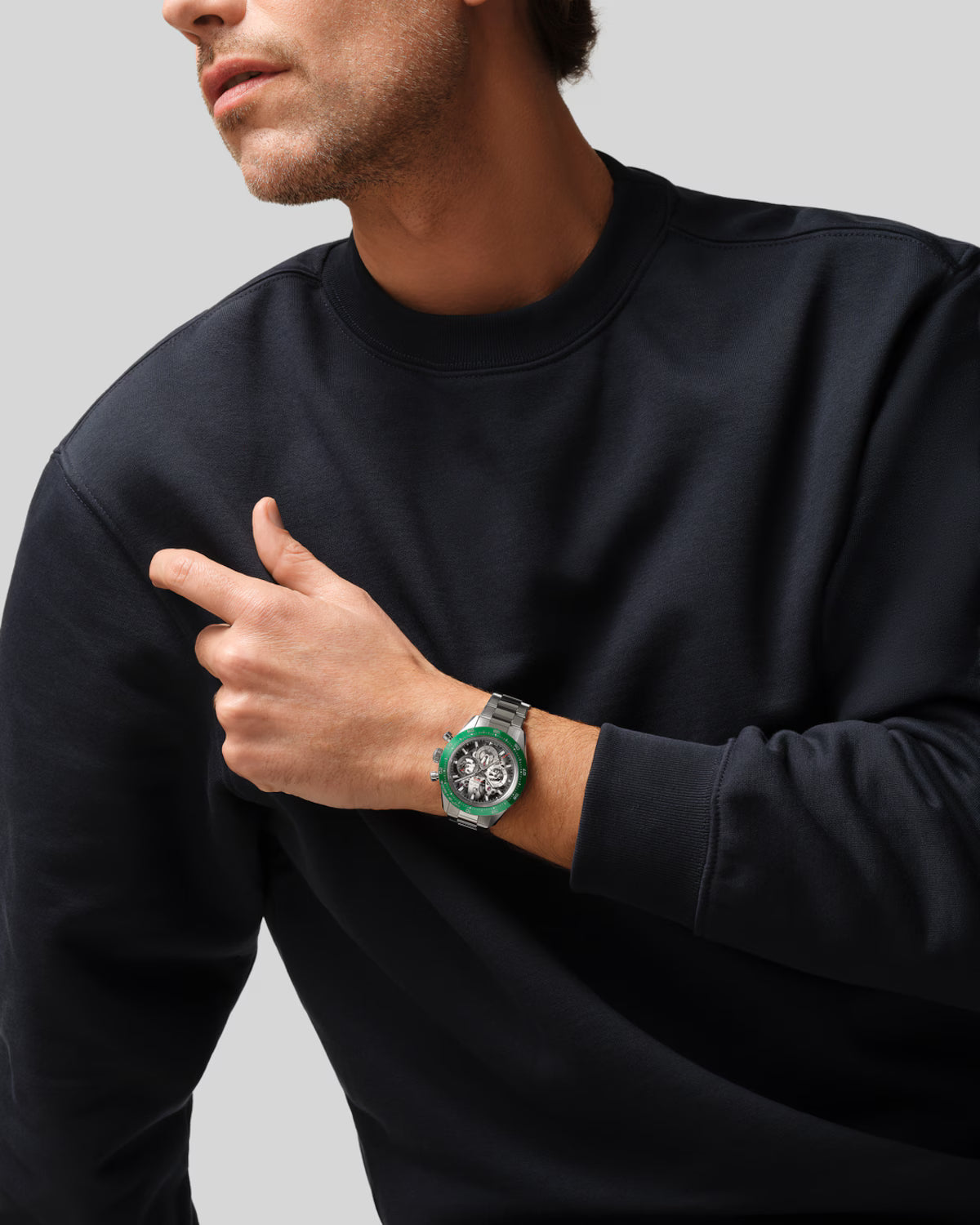Man wearing black crewneck sweatshirt with green and silver sports watch on wrist.