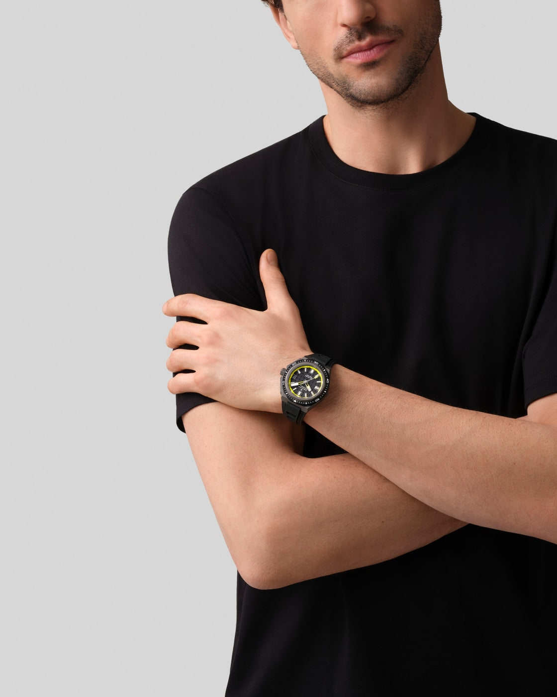 A man in a black t-shirt crosses his arms, showcasing the Zenith Defy Extreme Diver wristwatch in black and yellow against a plain background.