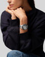 Silver chronograph watch with black dial and bezel on stainless steel bracelet, worn on wrist.