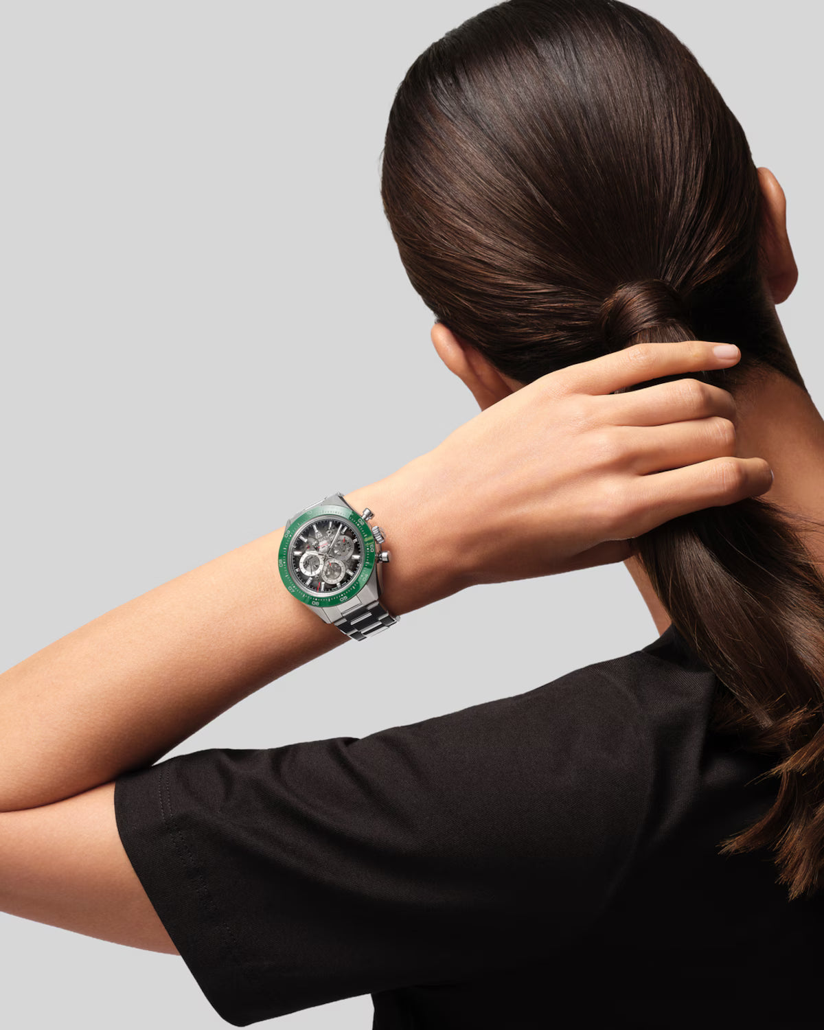 Sport watch with green bezel and metallic band worn on wrist.