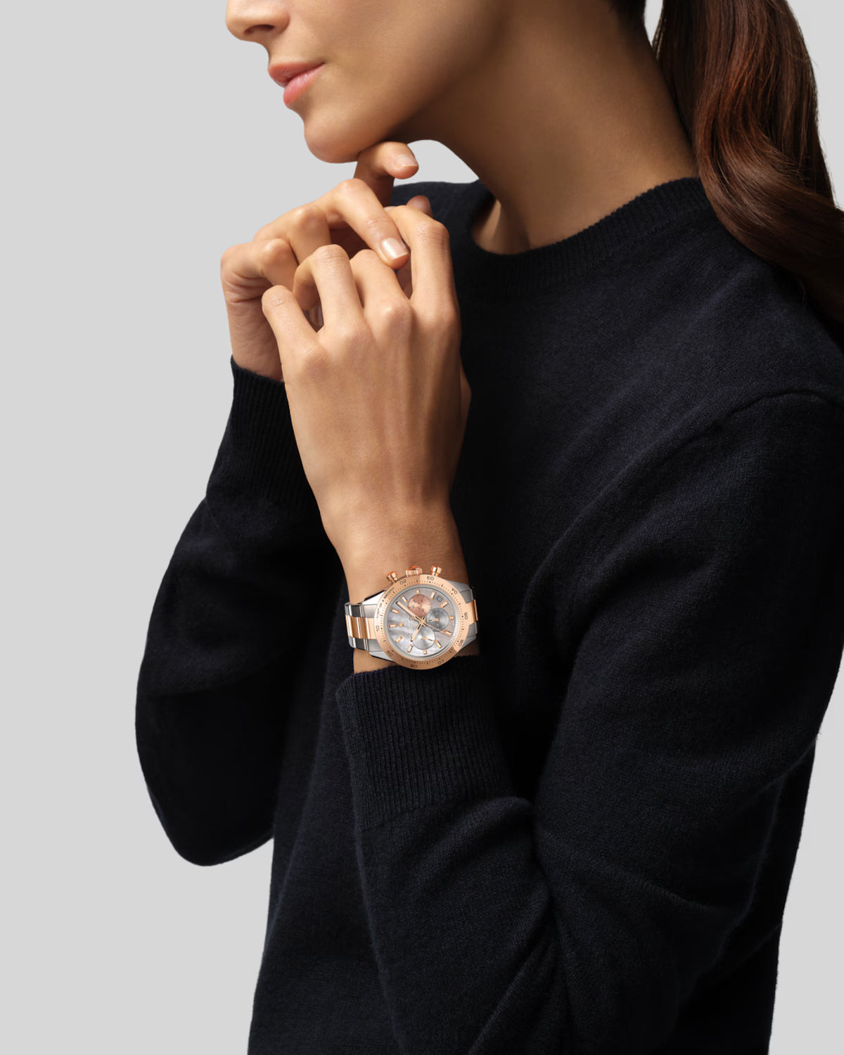 Woman wearing black sweater with rose gold and silver two-tone watch with chronograph dial on wrist.