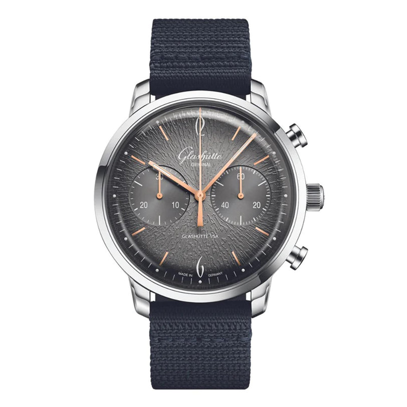 The Glashütte Original Sixties Chronograph Annual Edition is a stainless steel wristwatch with a textured gray dial, three subdials, rose gold hands, and a black fabric strap—an elegant homage to German watchmaking.