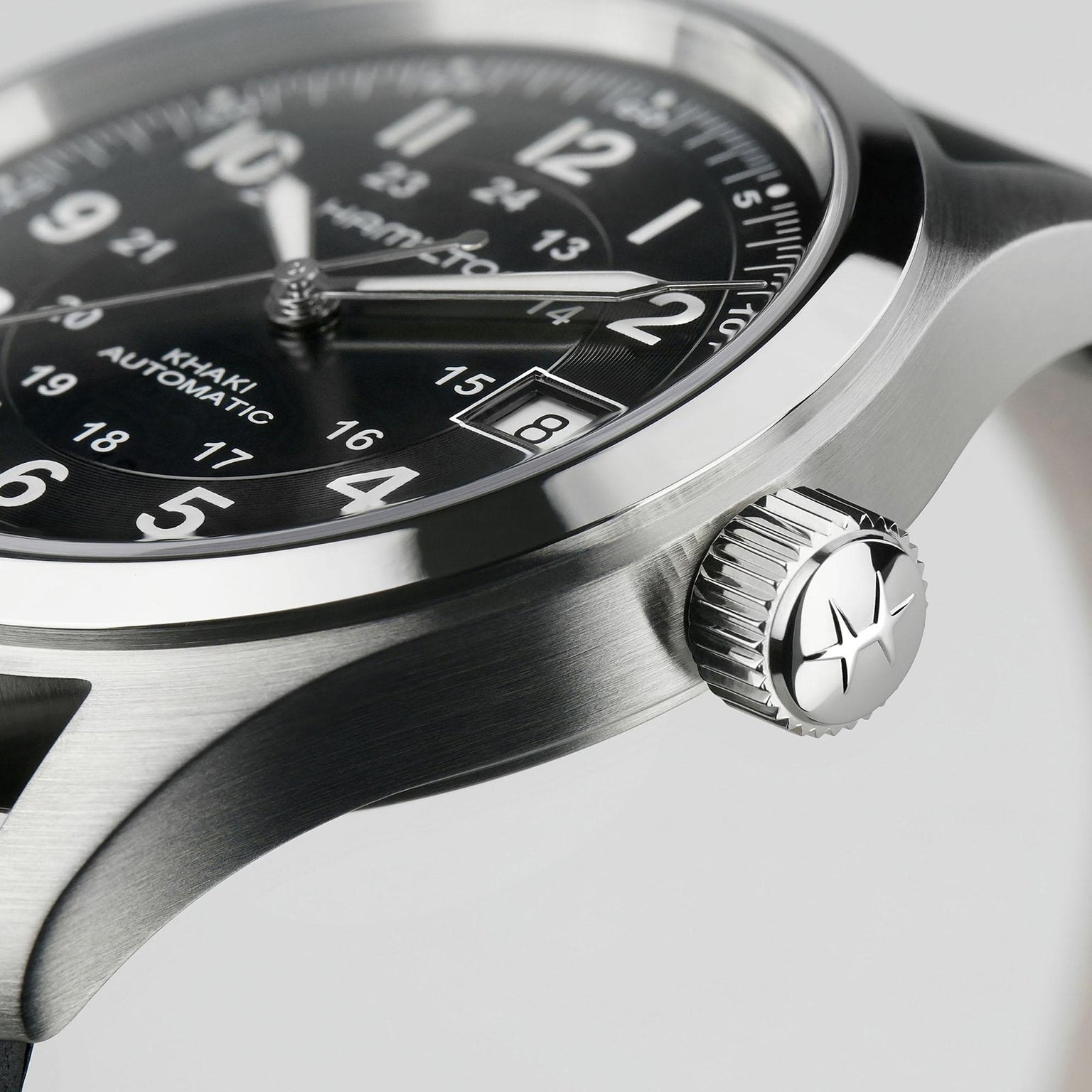 Close-up of the Hamilton Khaki Field Auto, a rugged, military-inspired watch with stainless steel case, black dial, white numerals, date window, and a textured crown featuring a star emblem.