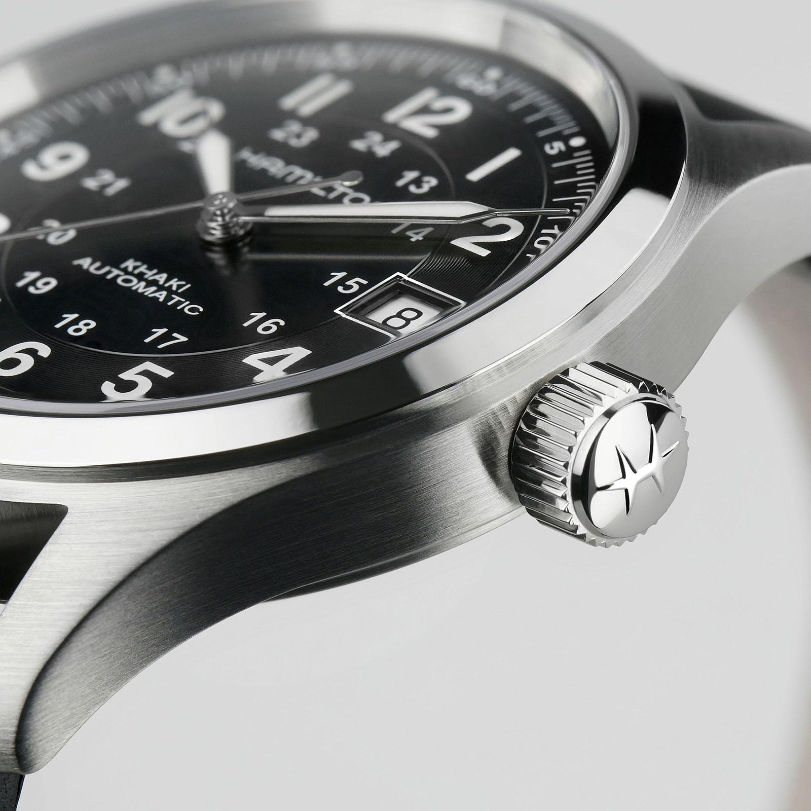 Close-up of the Hamilton Khaki Field Auto, a rugged, military-inspired watch with stainless steel case, black dial, white numerals, date window, and a textured crown featuring a star emblem.