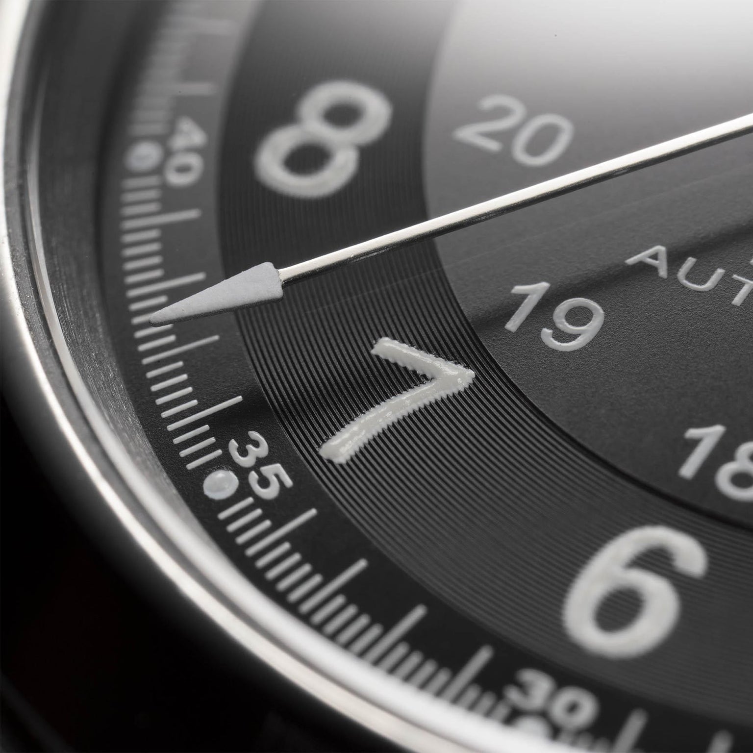 Close-up of a Hamilton Khaki Field King Auto watch face in black, displaying parts of the numbers 7, 8, and 20. A white hand points near the 37-minute mark and military time markings are visible.