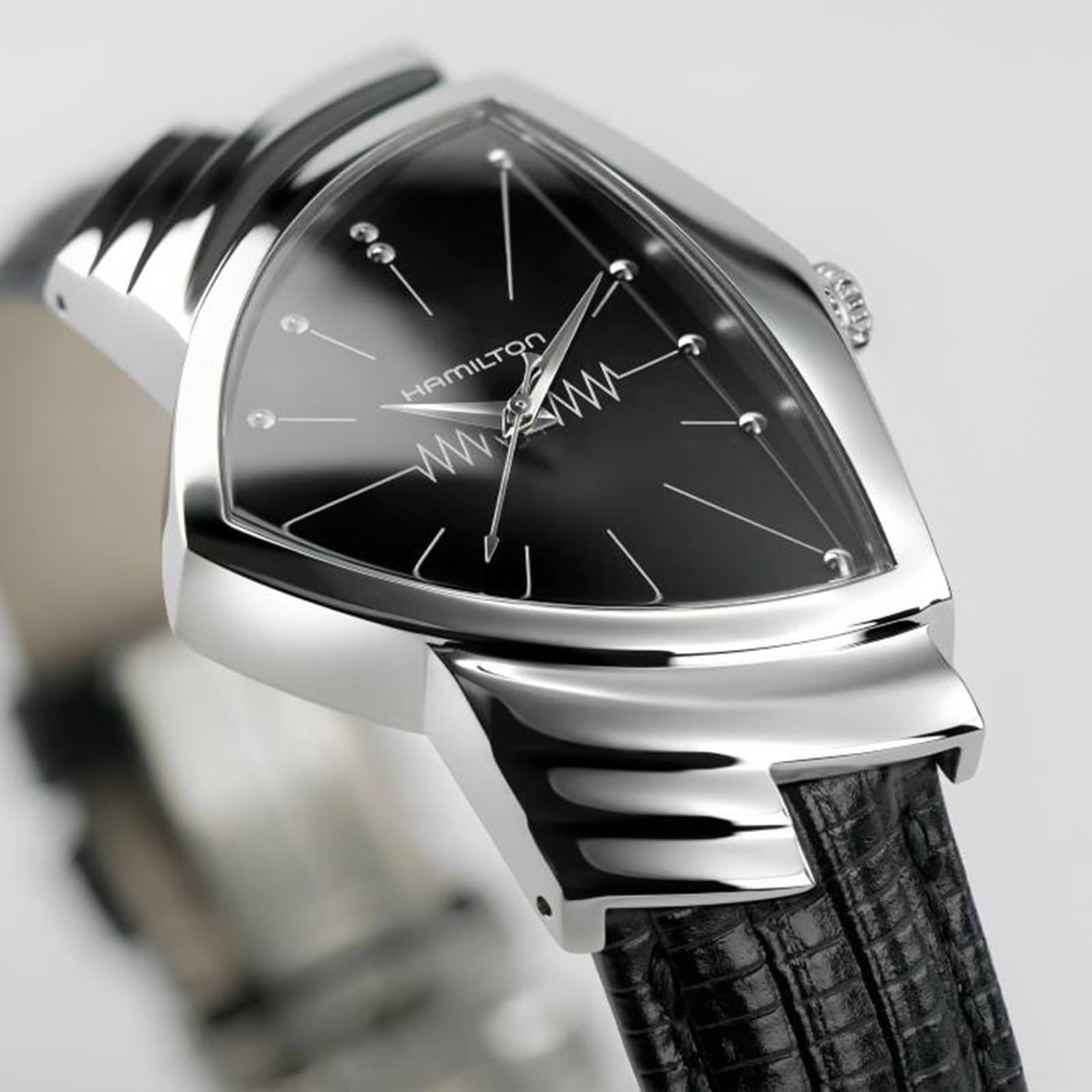 A close-up of the Hamilton Ventura Quartz wristwatch with a black triangular face, silver hour markers, and a textured black leather strap, highlighting its iconic Mid-Century Modern design.