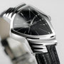A close-up of the Hamilton Ventura Quartz wristwatch with a black triangular face, silver hour markers, and a textured black leather strap, highlighting its iconic Mid-Century Modern design.