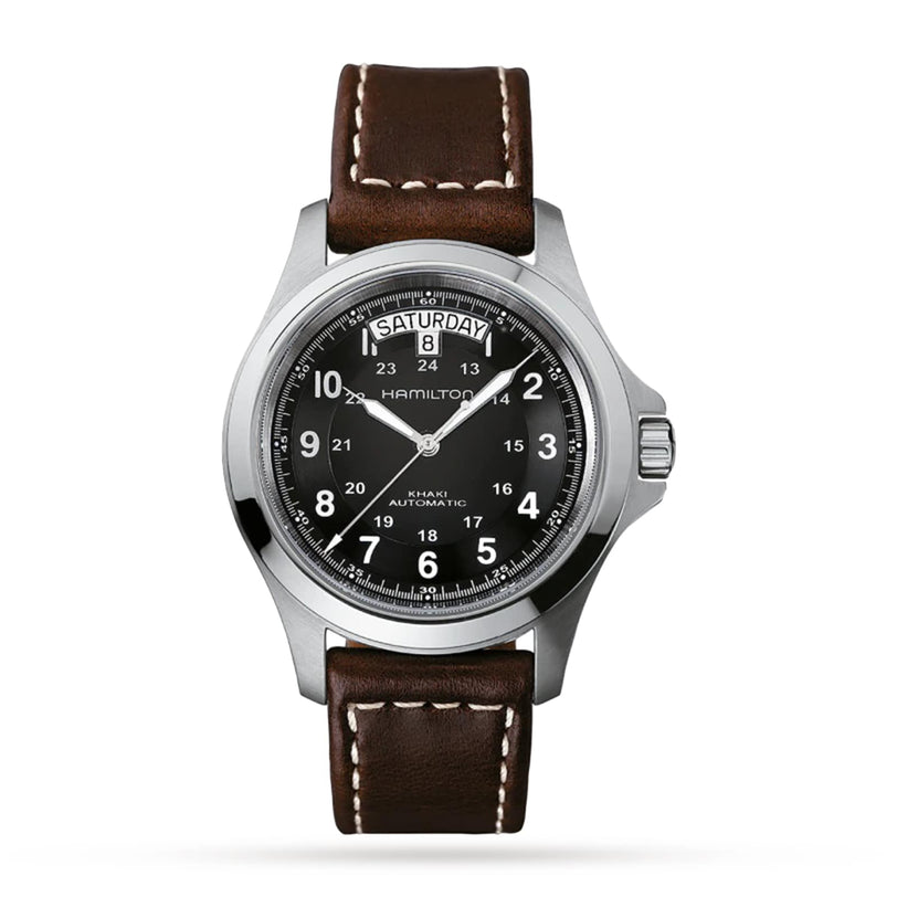 The Hamilton Khaki Field King Auto features a brown leather strap, black dial with white numerals and military time markings, crown protectors, and a day-date display at 12 o’clock.