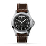 The Hamilton Khaki Field King Auto features a brown leather strap, black dial with white numerals and military time markings, crown protectors, and a day-date display at 12 o’clock.