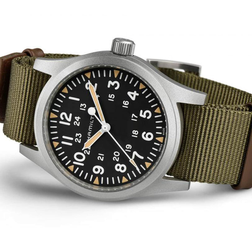 The Hamilton Khaki Field Mechanical 42mm is a soldier’s watch with a black dial, white numerals, green fabric strap, and both 12- and 24-hour markers for versatile timekeeping.
