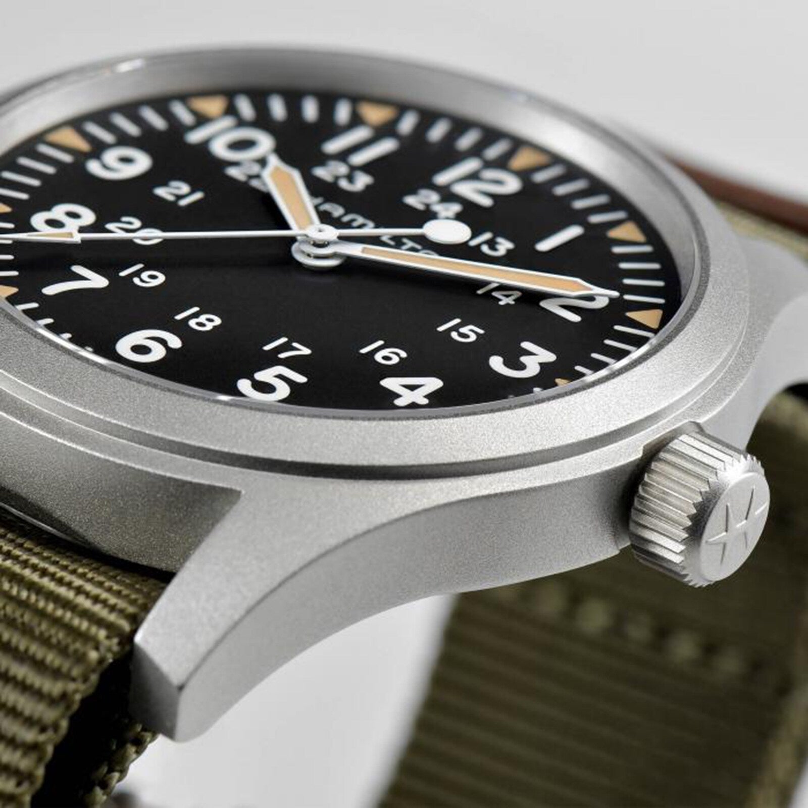 Close-up of the Hamilton Khaki Field Mechanical 42mm wristwatch, featuring a black dial with white numerals, luminous hands, green fabric strap, metal case with crown, and hand-wound H-50 movement.