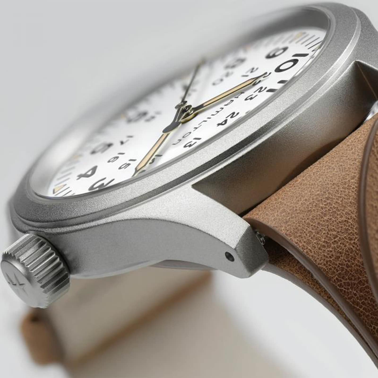 Close-up of the Hamilton Khaki Field Mechanical watch featuring a white dial with black numerals, silver case, and brown leather strap, highlighting the crown and part of the watch face.
