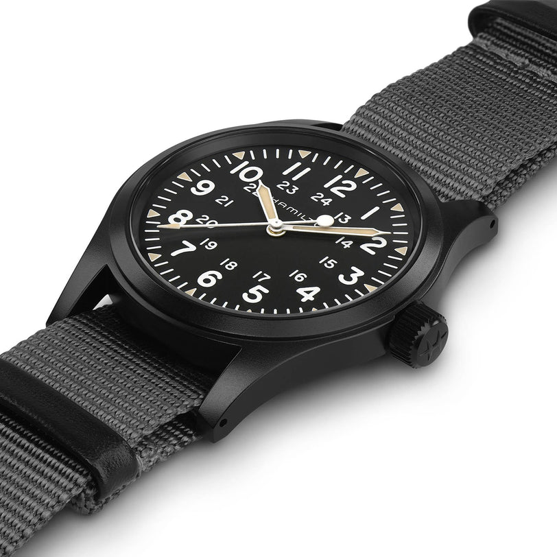A Hamilton Khaki Field Mechanical wristwatch with white Arabic numerals, a black NATO strap, and a matte black case is displayed at an angle on a white background.