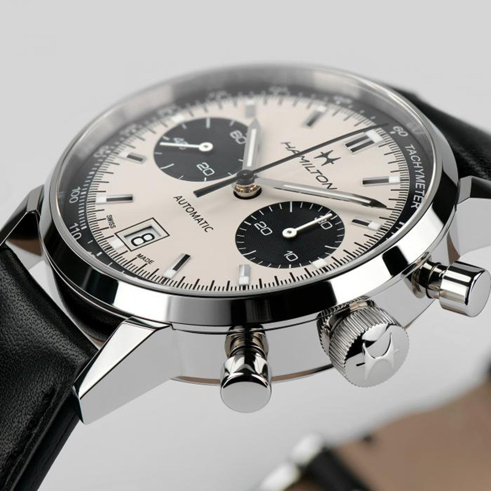 Close-up of the Hamilton American Classic Intra-Matic Auto Chrono, a silver chronograph wristwatch featuring a black leather strap and two subdials, shown against a light background.