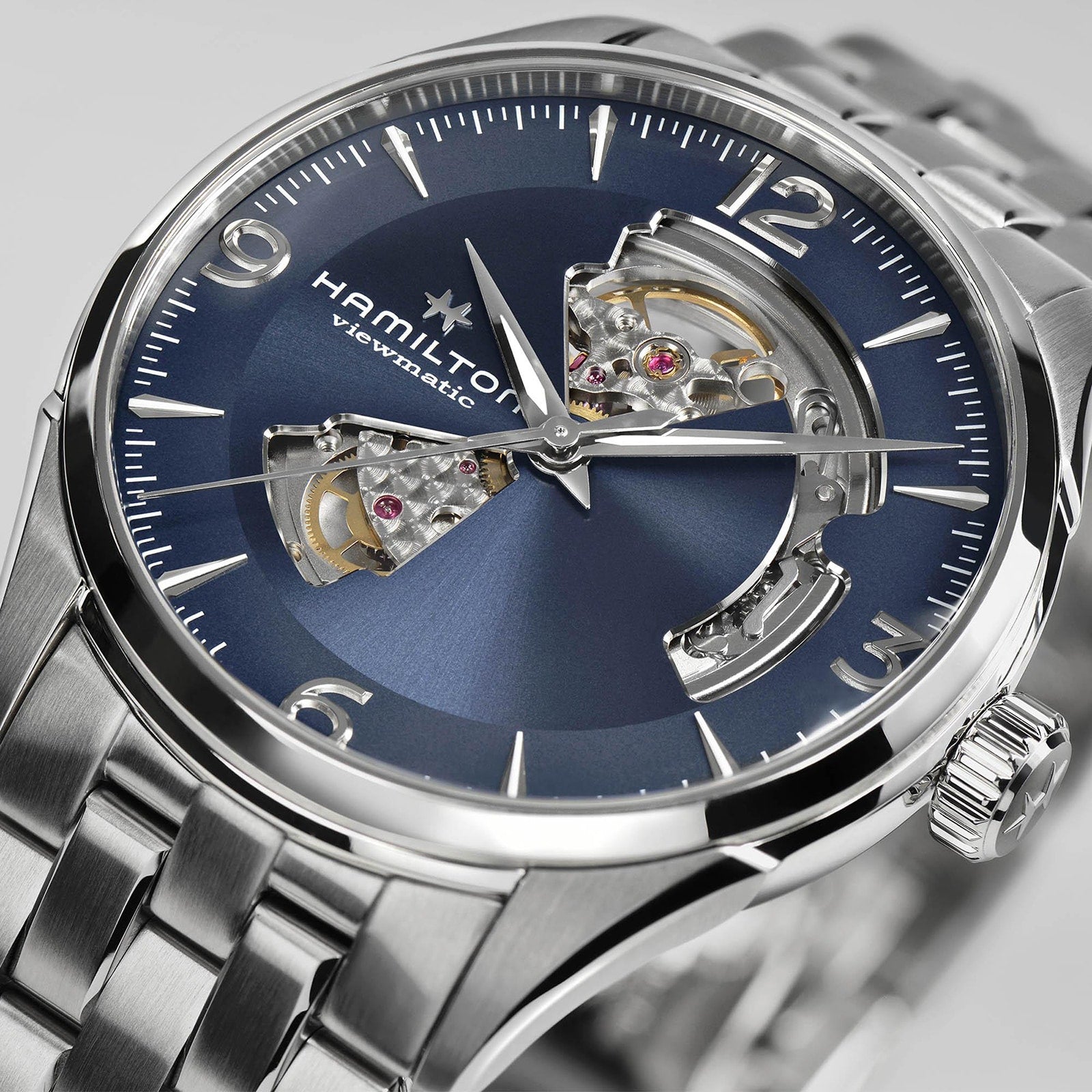 The Hamilton Jazzmaster Open Heart Auto is a stainless steel wristwatch featuring a blue dial, Swiss automatic movement, silver hands, and a metal link bracelet.
