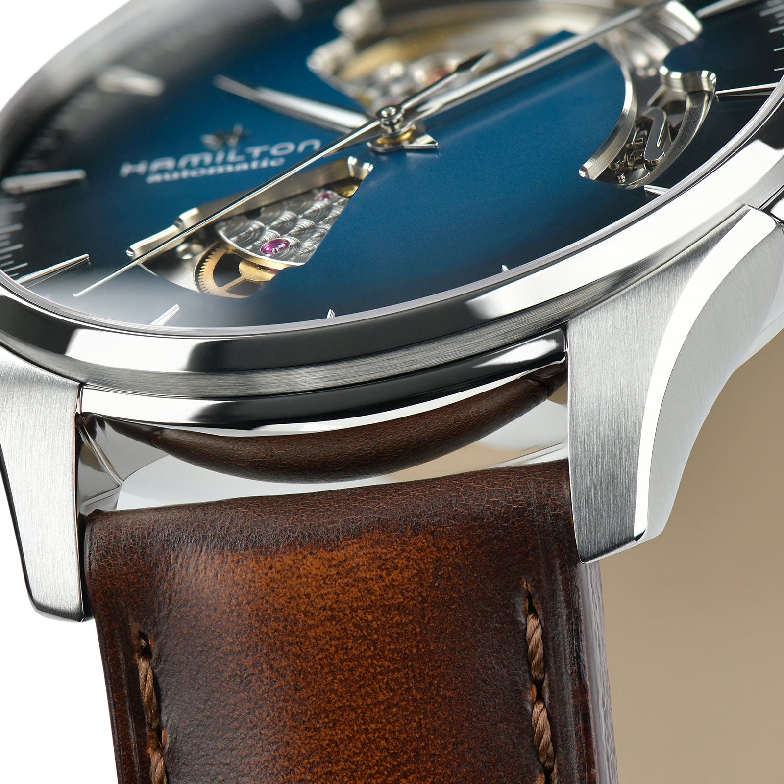 Close-up of the Hamilton Jazzmaster Open Heart Auto watch, featuring a smoked blue dial with visible movement, silver case, and brown leather strap in a modern style.