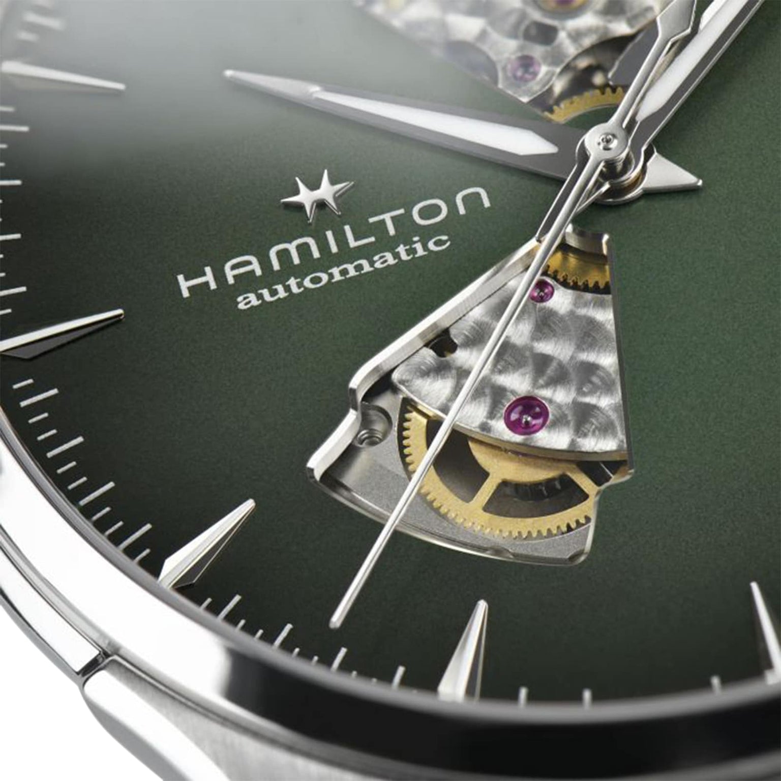 Close-up of the green Hamilton Jazzmaster Open Heart Auto watch face, featuring exposed gears, metallic hands, and a partially skeletonized smoked dial in a modern style.