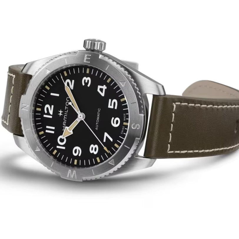 The Hamilton Khaki Field Expedition Auto is displayed on a white background, featuring a stainless steel case, Super-LumiNova® black dial with white numerals, and a brown leather strap.