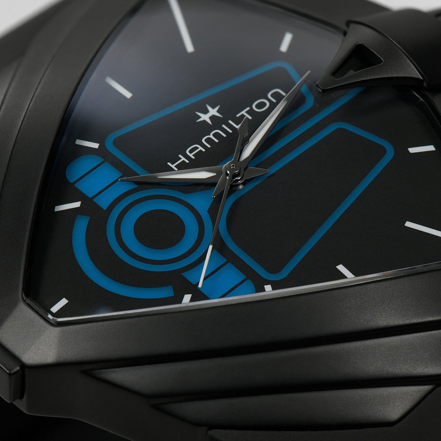 Close-up of the Hamilton Ventura XXL Bright Dune Limited Edition wristwatch, showcasing a black triangular case, blue geometric dial, and white hour, minute, and second hands.