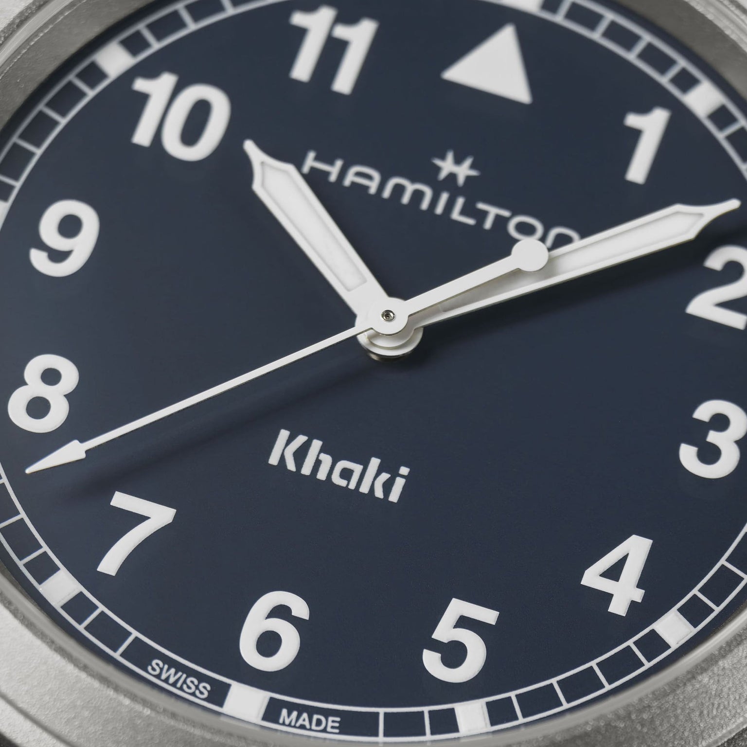 Close-up of the Hamilton Khaki Field Quartz 38mm watch face with silver hands, white numerals, and Hamilton, Khaki, and Swiss Made on a dark blue background, showcasing its military heritage.