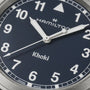Close-up of the Hamilton Khaki Field Quartz 38mm watch face with silver hands, white numerals, and Hamilton, Khaki, and Swiss Made on a dark blue background, showcasing its military heritage.