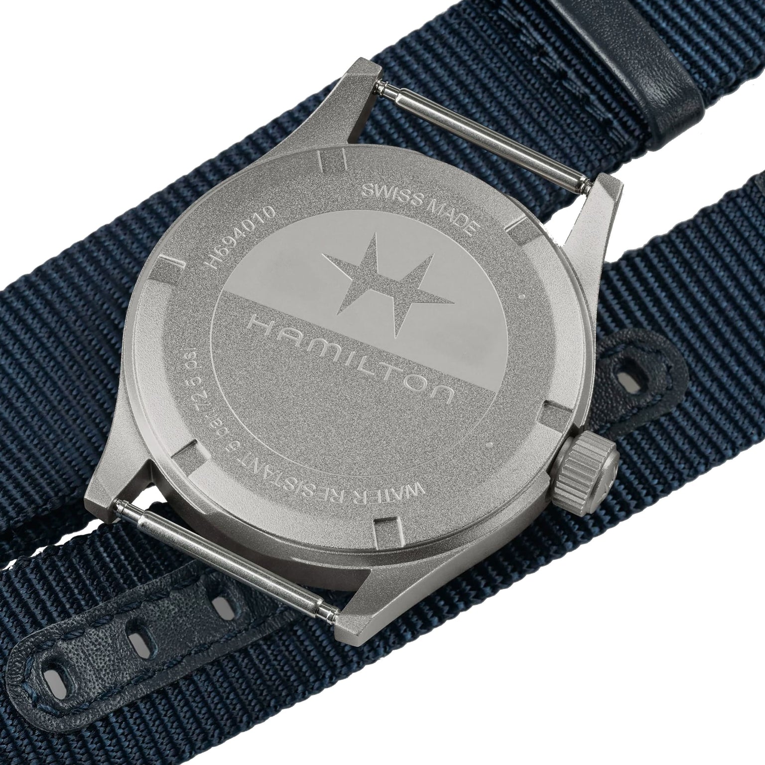 Close-up of the back of a Hamilton Khaki Field Quartz 38mm case with engravings, placed beside a blue NATO strap—highlighting its military-inspired design.