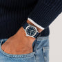 A person in a navy sweater and light blue jeans wears the Hamilton Khaki Field Quartz 38mm wristwatch with a dark blue dial and NATO strap, showcasing classic military heritage, on their left wrist.