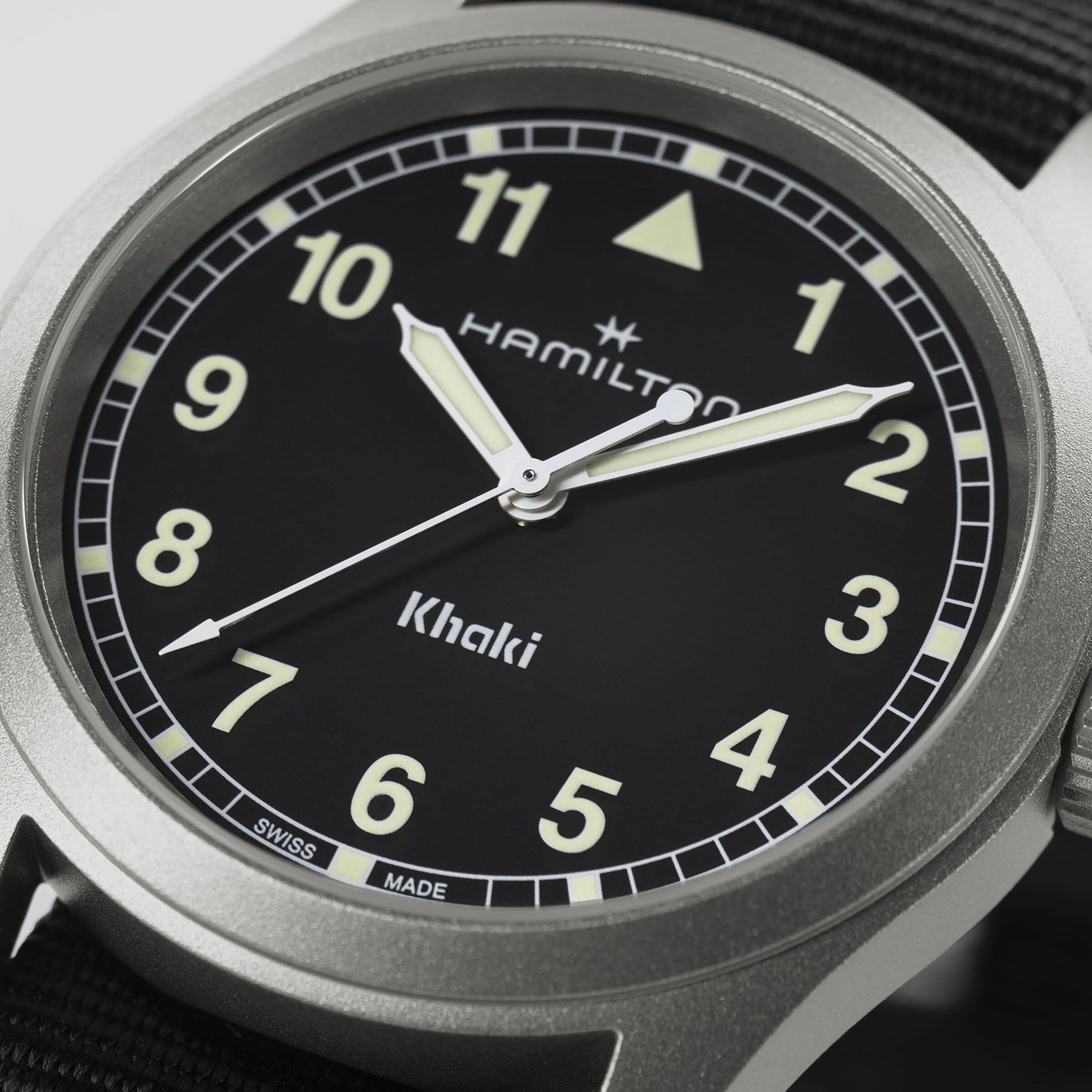 Close-up of a Hamilton Khaki Field Quartz watch showing 10:08, featuring a black dial and luminous hands.