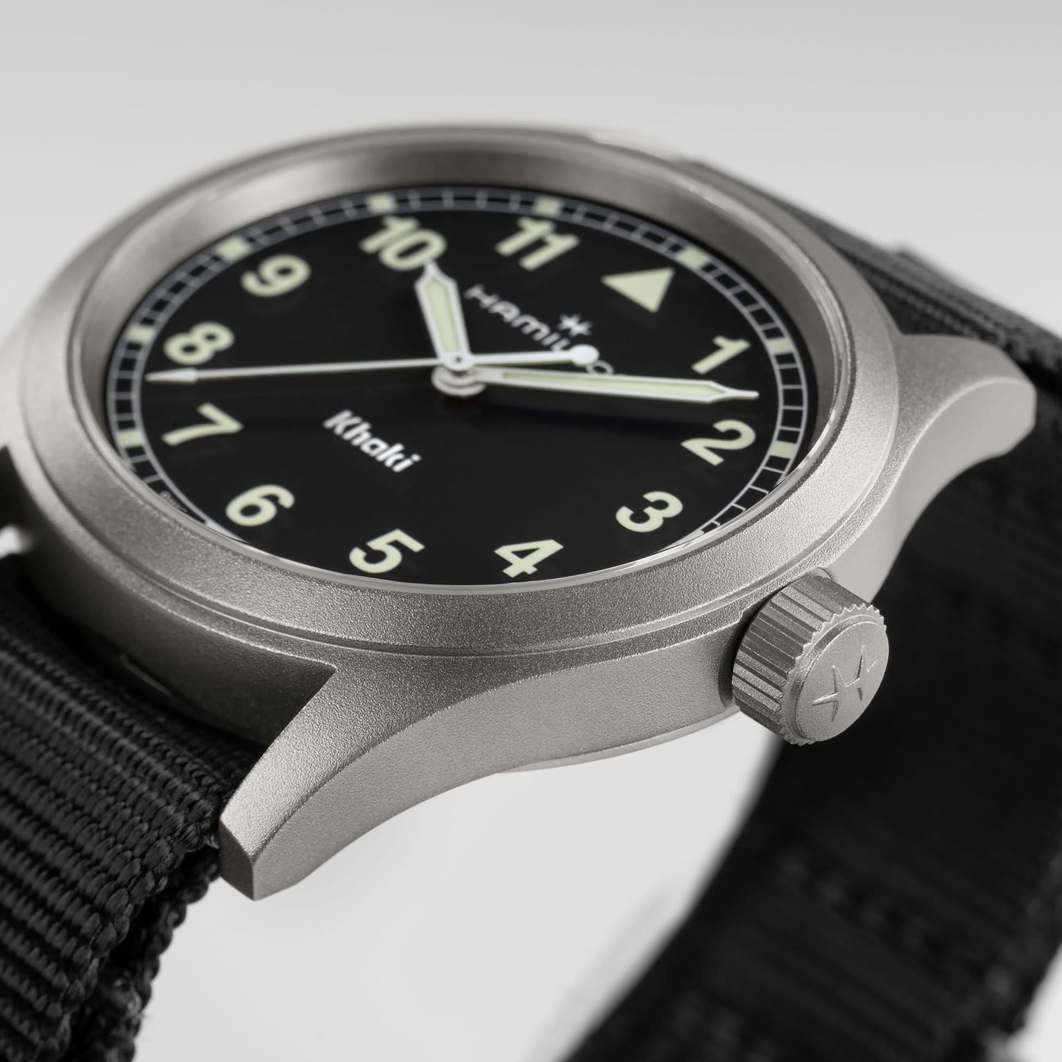 A close-up of the Hamilton Khaki Field Quartz wristwatch featuring a black face, white numbers, and a black fabric strap.