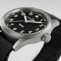 A close-up of the Hamilton Khaki Field Quartz wristwatch featuring a black face, white numbers, and a black fabric strap.