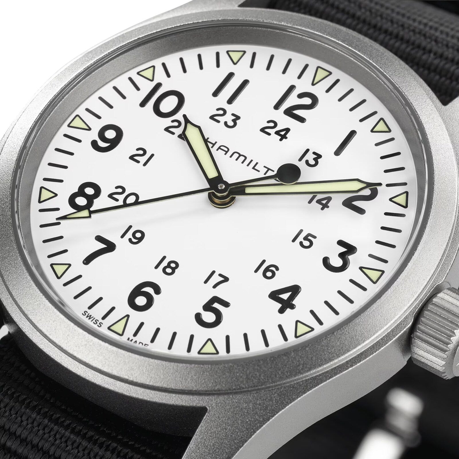 Close-up of the Hamilton Khaki Field Mechanical watch featuring a white dial with black numerals, 24-hour markings, luminous hands, and a rugged black NATO strap that highlights its military origins.