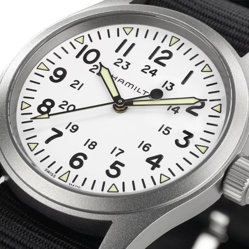 Close-up of the Hamilton Khaki Field Mechanical watch featuring a white dial with black numerals, 24-hour markings, luminous hands, and a rugged black NATO strap that highlights its military origins.