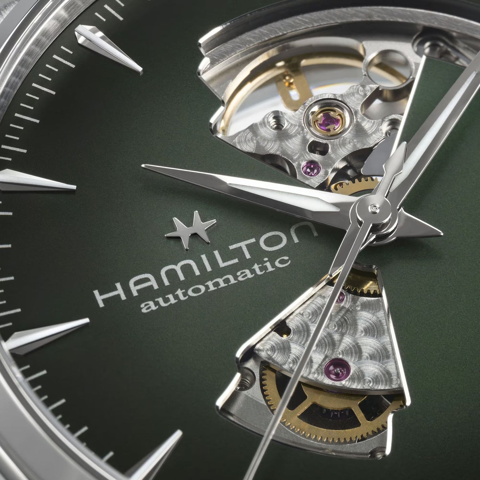 Close-up of the Hamilton Jazzmaster Open Heart Auto 42mm watch, featuring an open heart dial that reveals the inner gears, set against a green background.