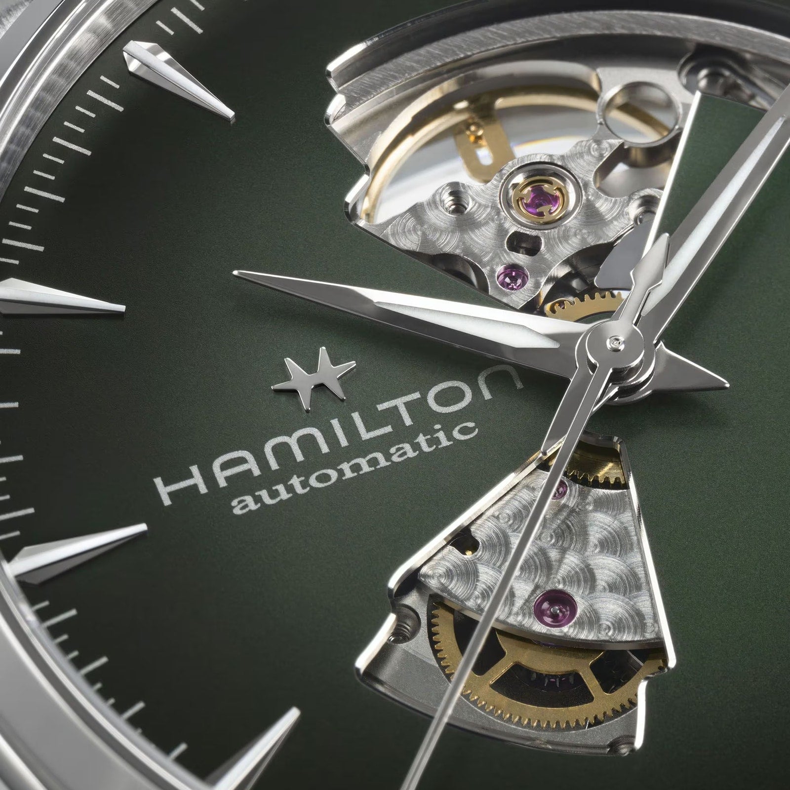 Close-up of the Hamilton Jazzmaster Open Heart Auto 42mm watch, featuring an open heart dial that reveals the inner gears, set against a green background.