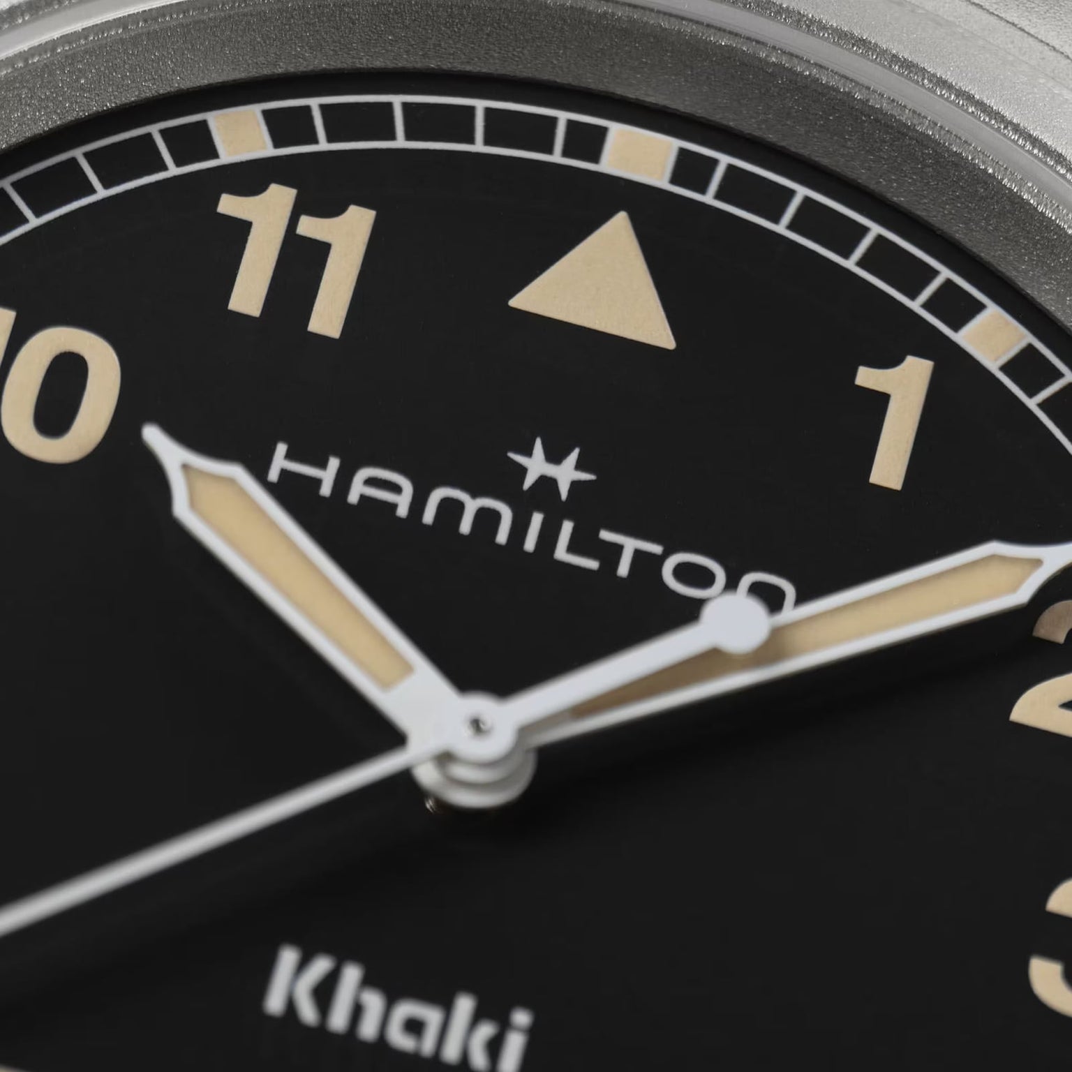 Close-up of a Hamilton Khaki Field Quartz 38mm watch face with beige hour markers and hands, showing partial view of 10 and 11.