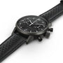 The Hamilton American Classic Intra-Matic Auto Chrono, a black chronograph wristwatch with a perforated leather strap, is photographed at an angle on a white background.