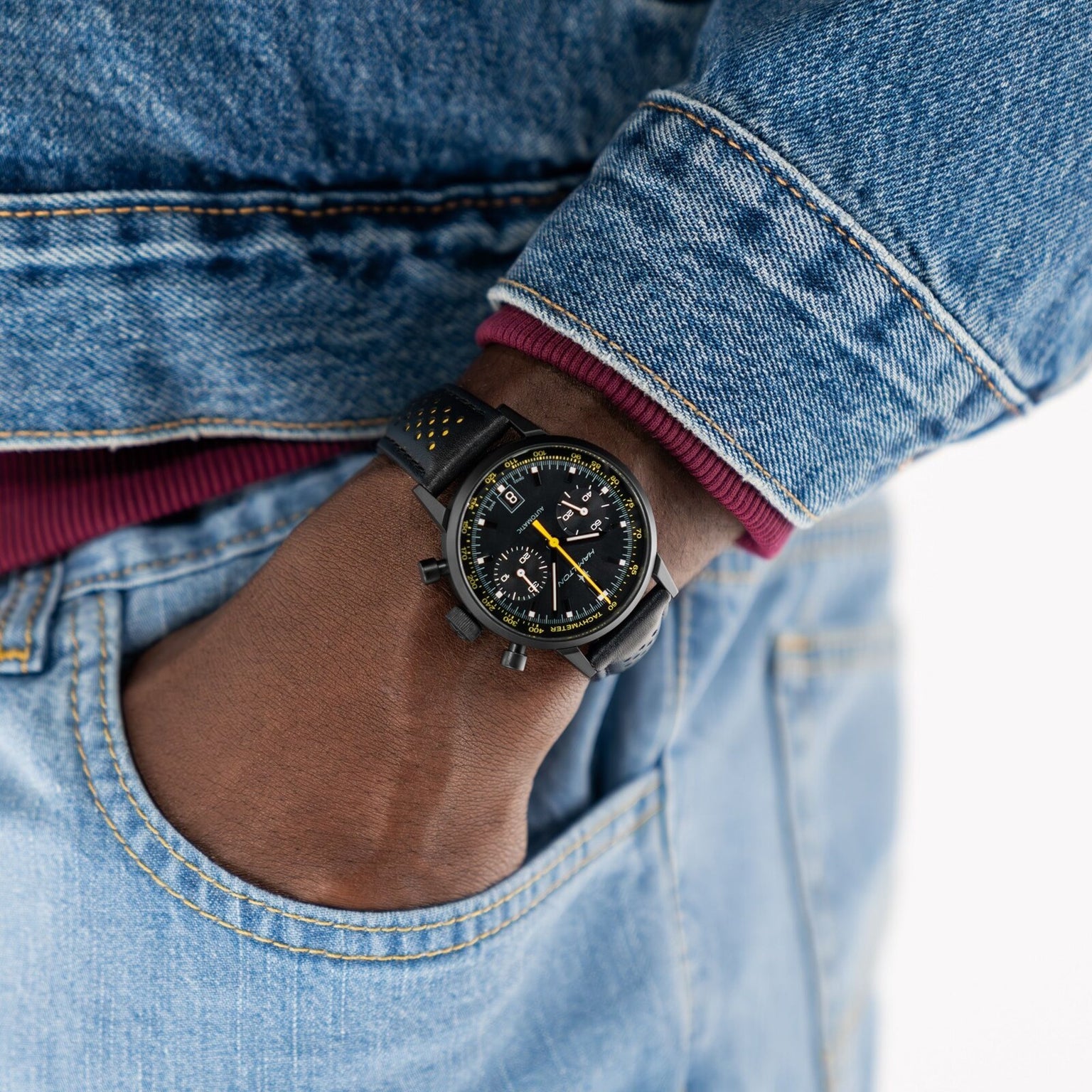A person in denim has their hand in their jeans pocket, wearing a Hamilton American Classic Intra-Matic Auto Chrono wristwatch.