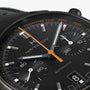 Close-up of a Hamilton American Classic Intra-Matic Auto Chrono watch in black with orange and white accents, featuring a date display at 4 o’clock.