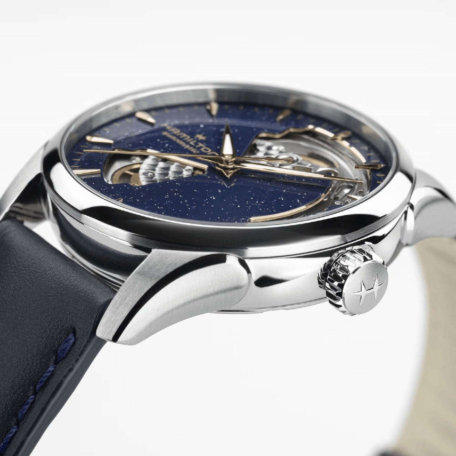 Close-up of the Hamilton Jazzmaster Open Heart Lady Auto, showcasing its blue star-patterned dial, visible automatic movement through a cutout, and silver case with a crown featuring a star emblem—a standout among luxury dress watches.